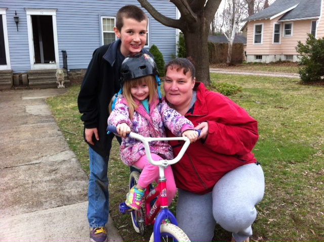 A woman and two children posing outdoors with a bike.